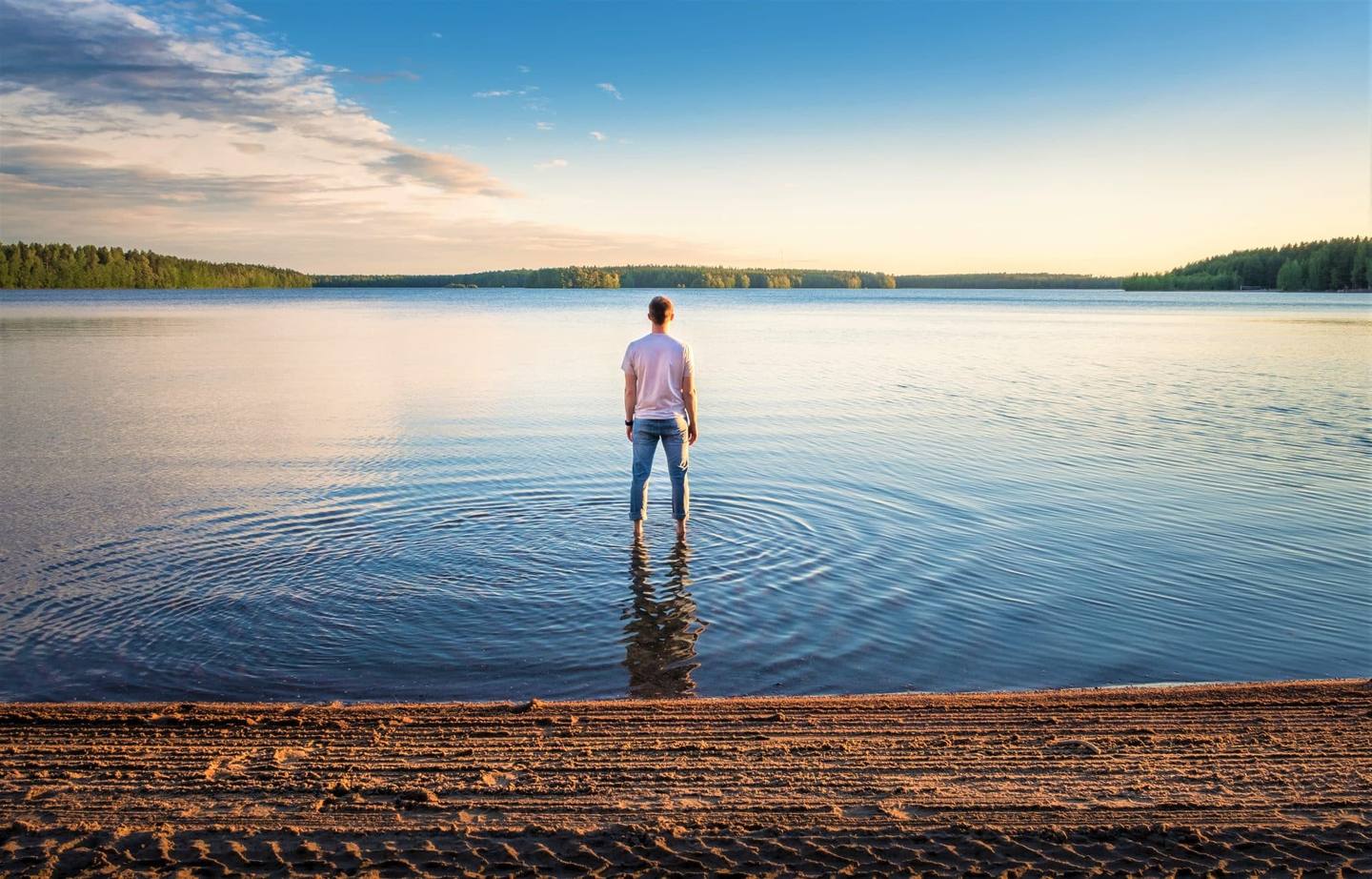 Homme debout dans l'eau lors d'une belle journée d'été avec lac idyllique et soirée tranquille en Finlande