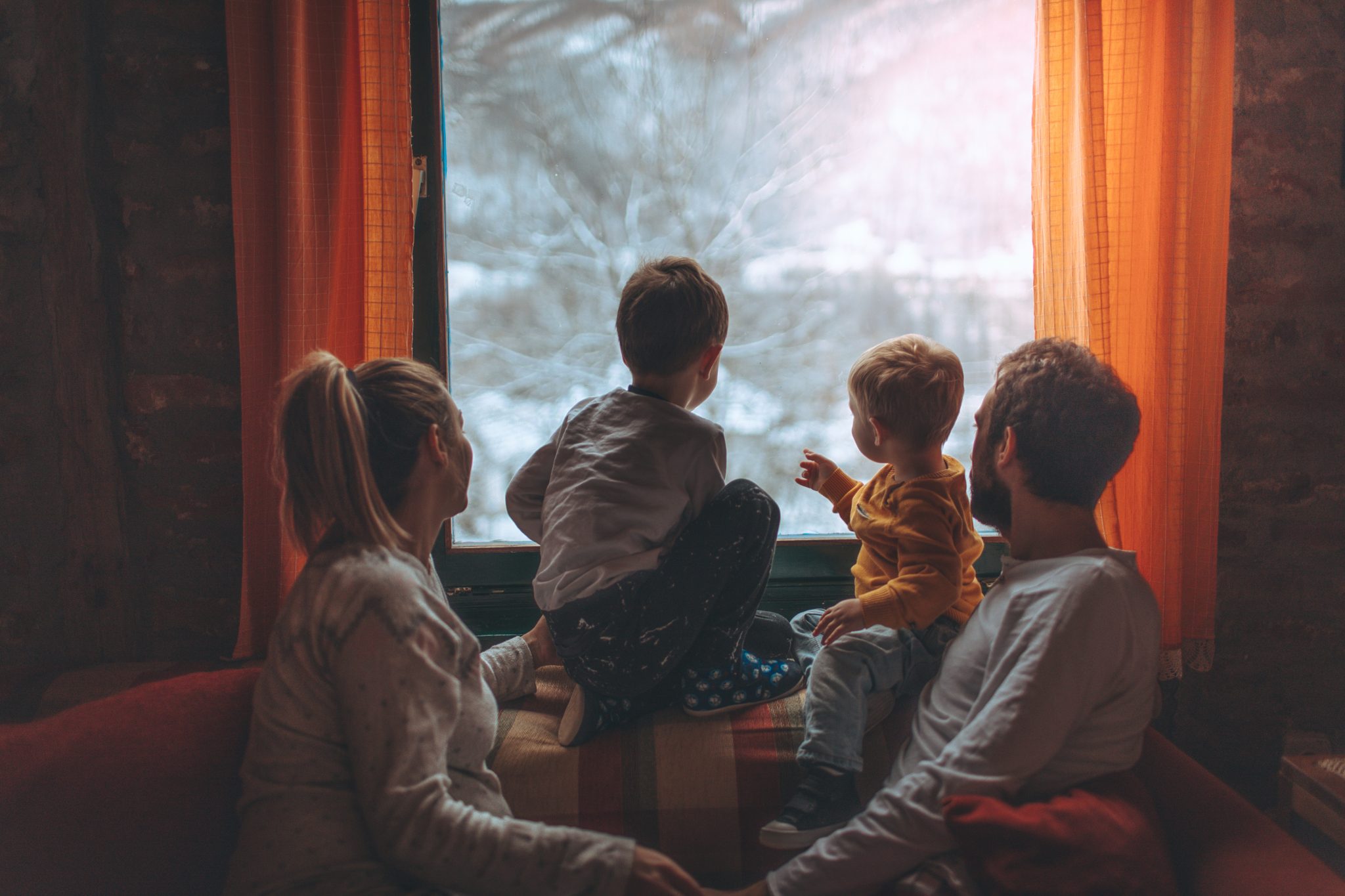 Famille devant la fenêtre de leur résidence de montagne entrain de regarder la neige