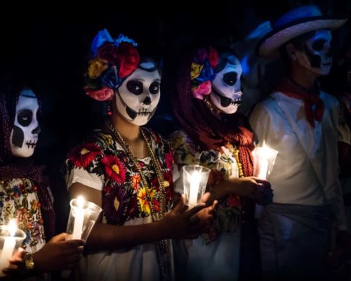 Merida, Cementerio General, Mexico - 31 October 2018: Three women with Catrina customes and man with white cowboy dress with skull make-up holding candels at the parade for dia de los muertos at the Festival Des Las Animas