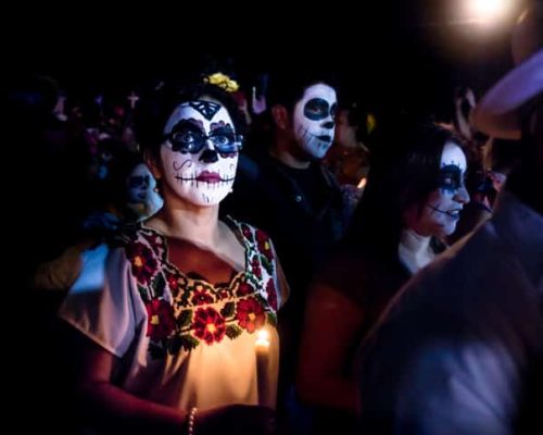 Merida, Cementerio General, Mexico - 31 October 2018: Woman with skull and spiderweb make-up and glasses and dress with traditional mexican flowers surrounded by costumed people at the parade for dia de los muertos at the Festival Des Las Animas