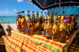 Stand au marché de Sainte Anne, avec des bouteilles de rhum arrangé colorées et la vue sur la plage et la mer