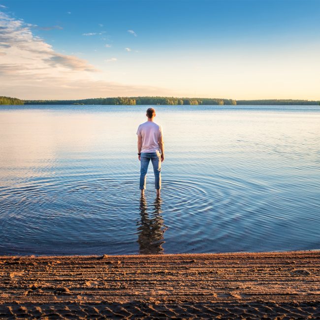 Homme debout dans l'eau lors d'une belle journée d'été avec lac idyllique et soirée tranquille en Finlande