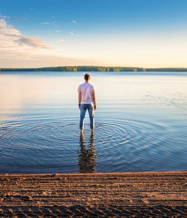 Homme debout dans l'eau lors d'une belle journée d'été avec lac idyllique et soirée tranquille en Finlande