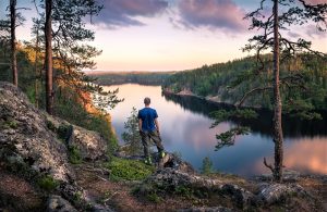 Incontournables de la Finlande : Randonneur se tenant au sommet de la colline devant un beau paysage idyllique à Mäntyharju, Finlande.